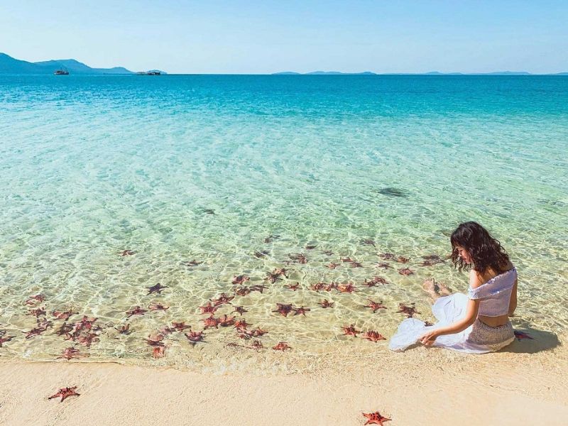International tourists admiring red starfish on the clear waters of Rach Vem beach during an excursion from the famous Corona Casino Phu Quoc