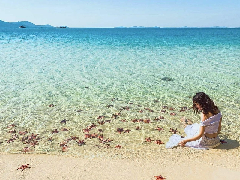 A tourist observing red starfish on Starfish Beach in Phu Quoc