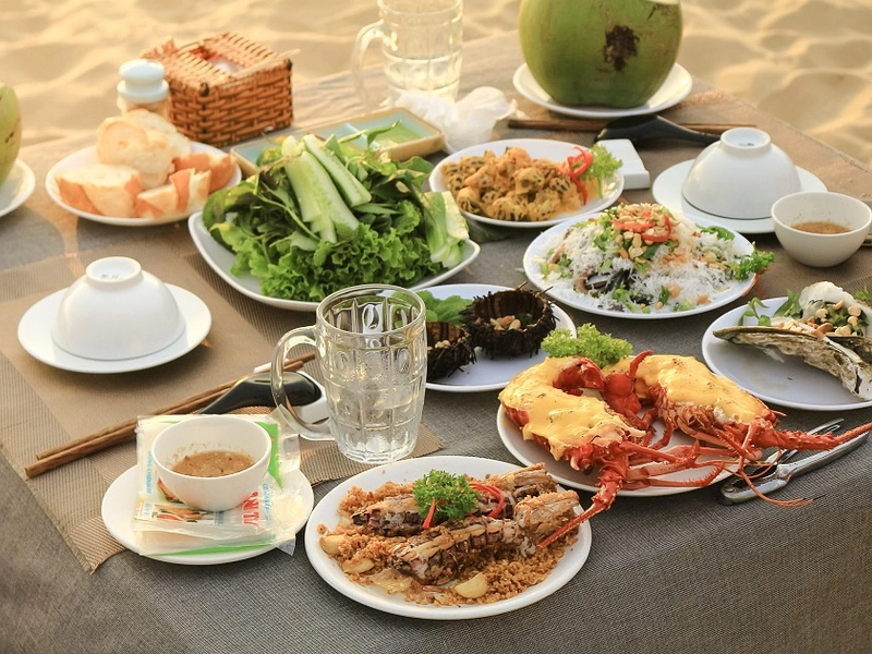 Beachfront dining table showing grilled cheese lobsters and mantis shrimp at sunset near Corona Resort & Casino Phu Quoc