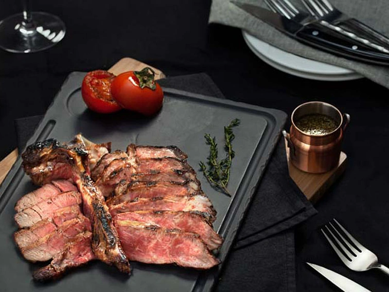 An elegant medium-rare sliced T-bone steak presented on a dark slate platter, representing fine dining steak in Phu Quoc at Pink Pearl near Corona Resort & Casino Phu Quoc