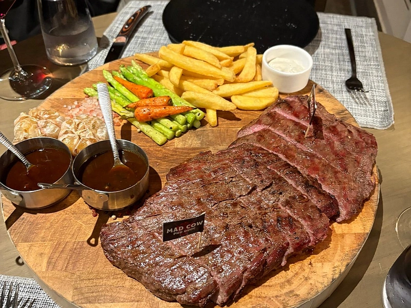 A perfectly sliced grilled steak served on a wooden board with a Mad Cow Phu Quoc flag, a signature dish for steak in Phu Quoc near Corona Resort & Casino Phu Quoc