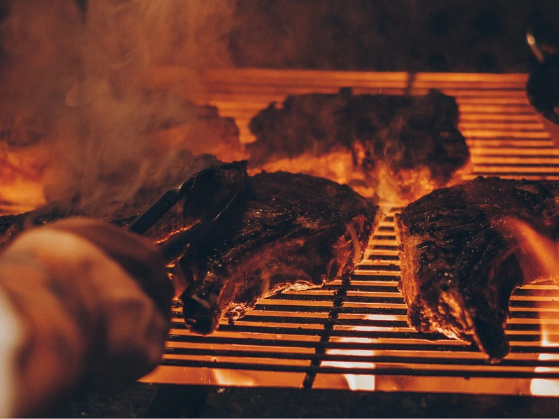 Premium cuts of imported beef sizzling on a hot grill over intense flames, showing the preparation of steak in Phu Quoc near Corona Resort & Casino Phu Quoc
